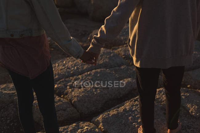 Baixa seção de casal de mãos dadas enquanto de pé na praia — Fotografia de Stock