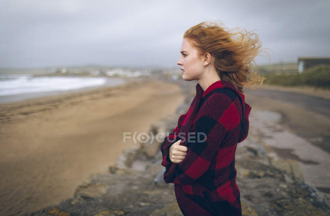 Продумана руда жінка стоїть з обіймами, схрещеними на пляжі . — стокове фото
