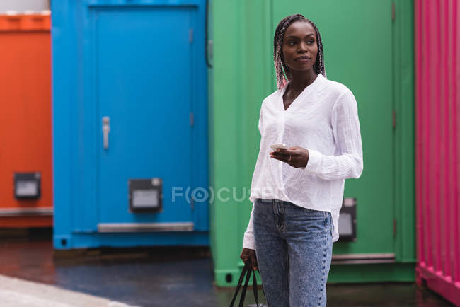 Fashionable young woman with mobile phone looking away — Stock Photo