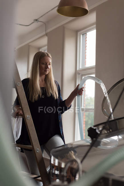 Beautiful female worker filling water in distillery tank at factory — Stock Photo