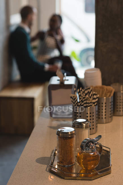 Agitadores de sal y pimienta en el mostrador y pareja en el fondo en la cafetería - foto de stock