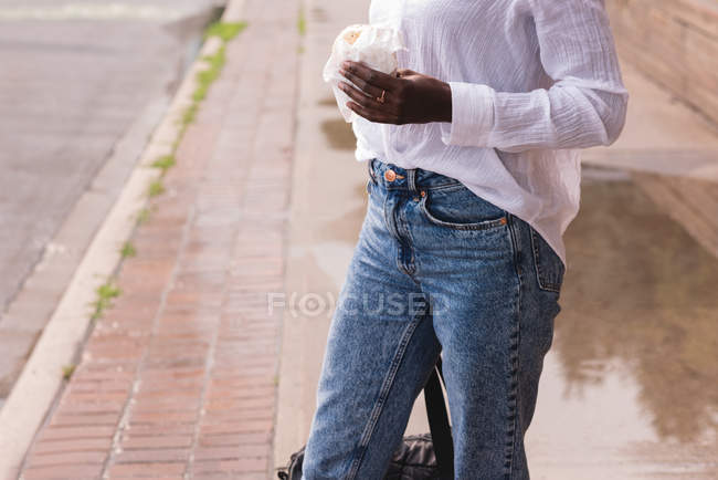 Mid section of woman with burger walking on sidewalk — Stock Photo