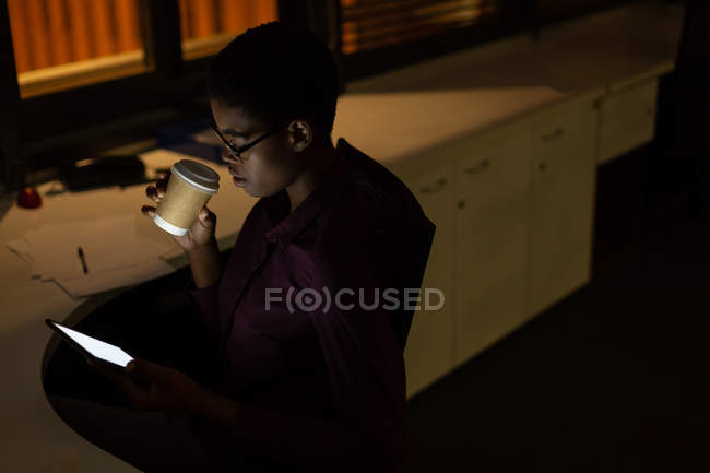 Weibliche Führungskraft beim Kaffeetrinken mit digitalem Tablet in der Nacht im Büro — Stockfoto