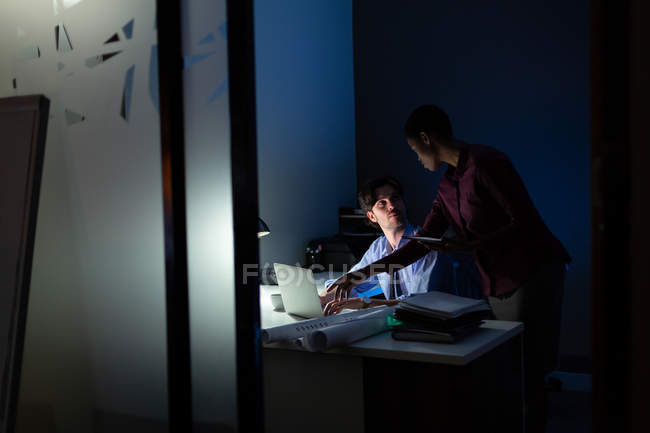 Руководители обсуждают за ноутбуком в офисе ночью — стоковое фото