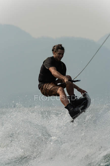 Jeune homme éclaboussant l'eau tout en wakeboard dans la rivière — Photo de stock