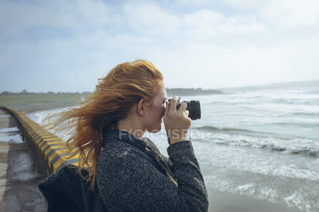 Donna rossa che scatta foto con macchina fotografica in spiaggia . — Foto stock