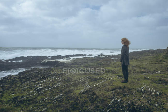 Thoughtful redhead woman standing in rocky beach. — Stock Photo