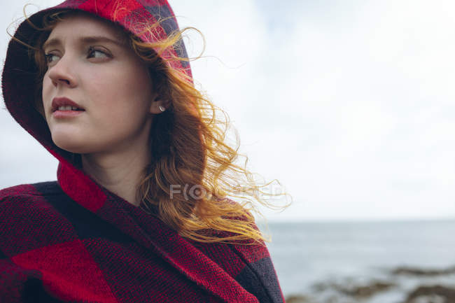 Nachdenkliche rothaarige Frau steht an windigem Strand. — Stockfoto