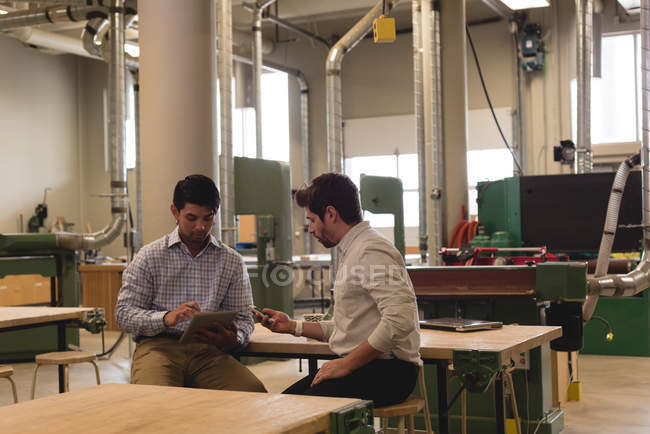 Two craftsmen using digital tablet and mobile phone in workshop — Stock Photo