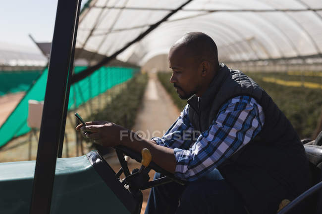 Человек, использующий мобильный телефон, сидя на тракторе на черничной ферме — стоковое фото