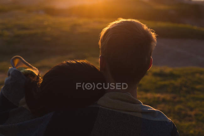 Couple romantique assis sur la plage pendant le coucher du soleil — Photo de stock
