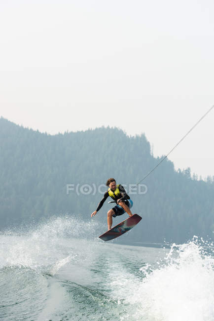 Male wakeboarder riding waves of woodland river — Stock Photo