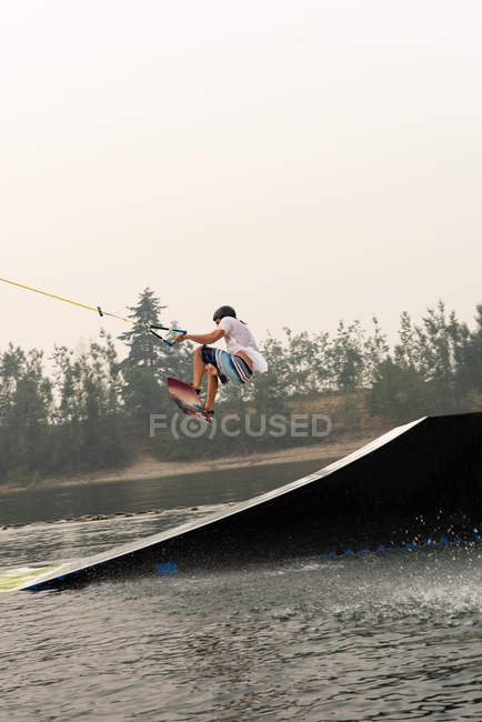 Mid adult man wakeboarding from ramp in river water — Stock Photo