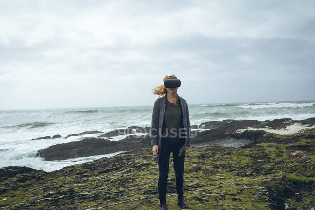 Mujer pelirroja usando auriculares de realidad virtual en la playa . - foto de stock