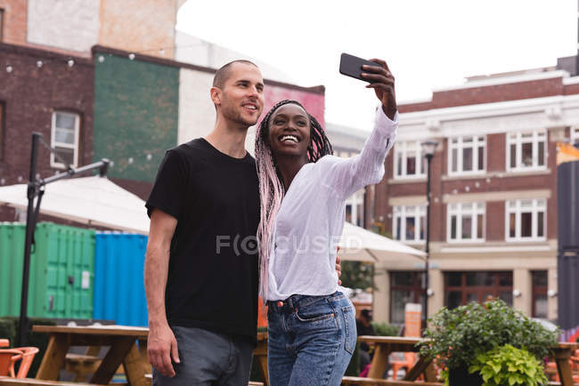 Jeune couple souriant prenant selfie contre les bâtiments — Photo de stock