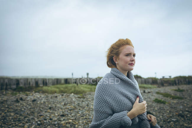 Продумана руда жінка в сірому піджаку, що стоїть біля пляжу . — стокове фото