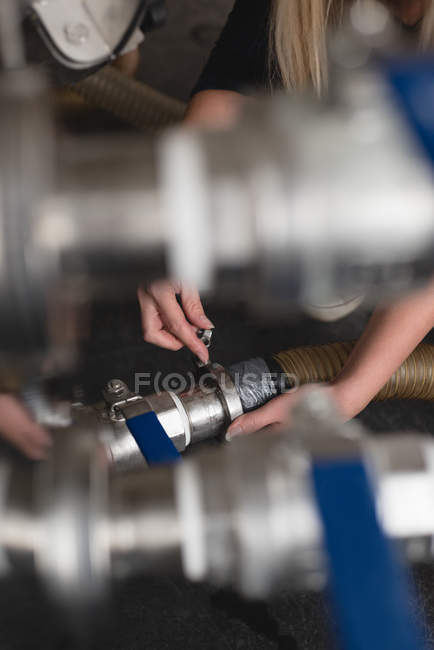 Mid section of female worker checking pipe of distillery tank — Stock Photo