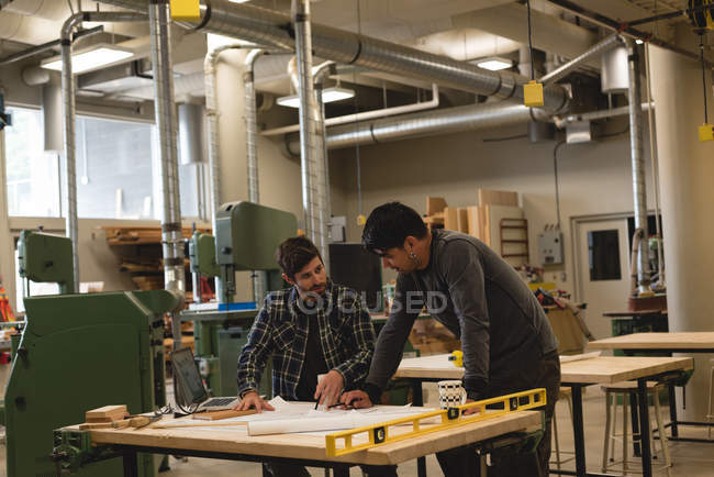 Zwei Handwerker diskutieren in Werkstatt über Bauplan — Stockfoto