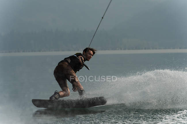 Jeune homme wakeboard dans la rivière avec éclaboussures d'eau — Photo de stock