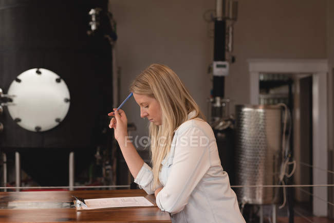 Beautiful female worker writing on clipboard in factory — Stock Photo