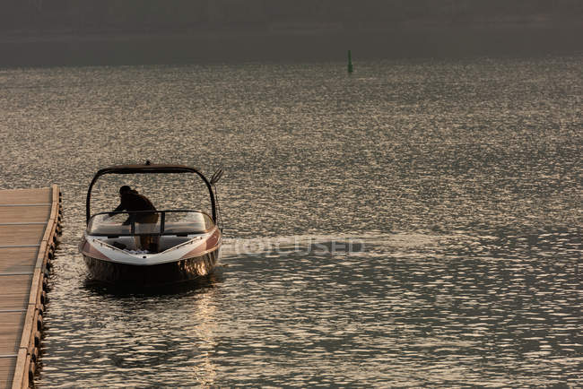 Uomo irriconoscibile in piedi su motoscafo nel fiume al tramonto — Foto stock