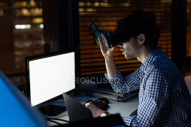 Male executive using virtual reality headset in office at night — Stock Photo