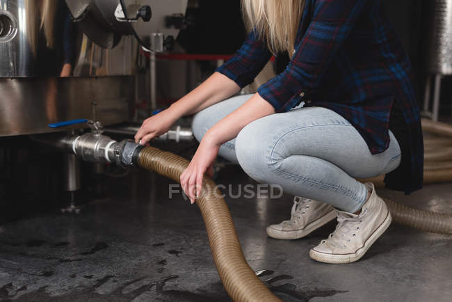 Travailleuse contrôlant le tuyau du réservoir de distillerie en usine — Photo de stock