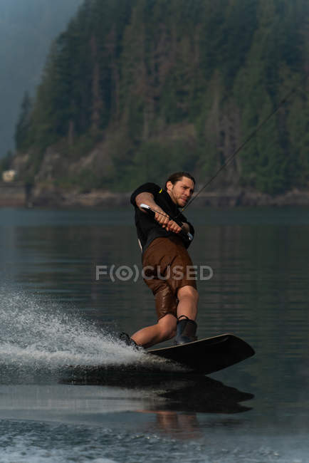 Jeune homme éclaboussant l'eau tout en wakeboard dans la rivière — Photo de stock
