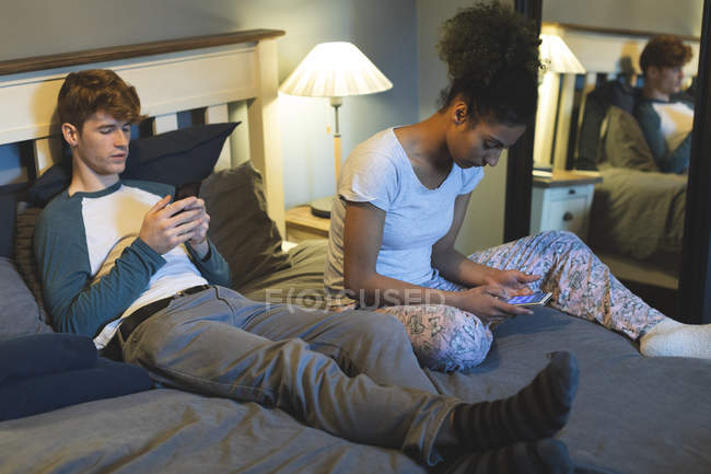 Пара с помощью мобильных телефонов в спальне на дому — стоковое фото