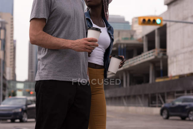 Sección media de pareja con tazas de café caminando por la calle - foto de stock