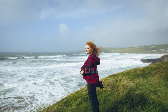 Thoughtful redhead woman standing with arms crossed in the beach. — Stock Photo
