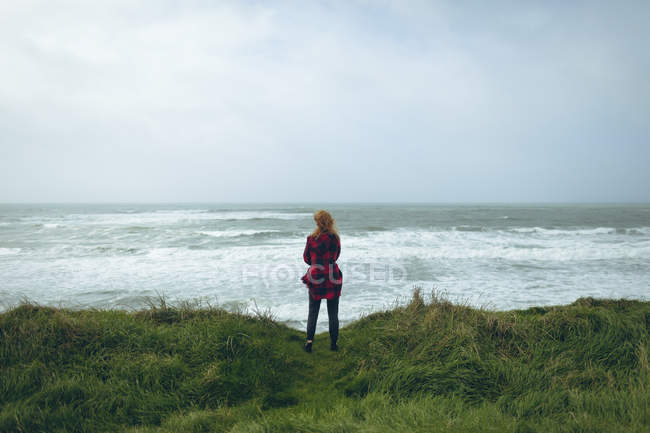 Vista trasera de mujer pelirroja de pie en la playa cubierta de hierba . - foto de stock