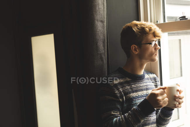 Мужчина пьет кофе, глядя в окно дома — стоковое фото
