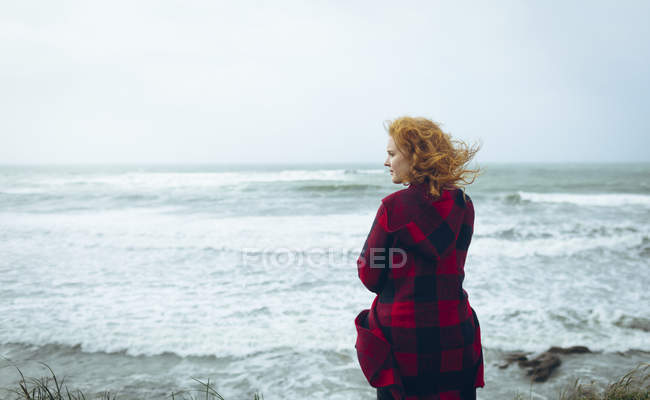 Вид спереду руда жінка стоїть на пляжі біля води . — стокове фото