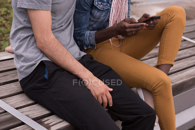 Mittelteil des Paares sitzt auf Bank und benutzt Mobiltelefon — Stockfoto