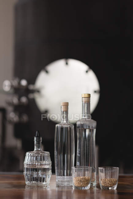 Close-up de garrafas de cervejaria e grãos de trigo em copos — Fotografia de Stock
