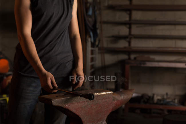 Mid section of female metalsmith holding tool in factory — Stock Photo