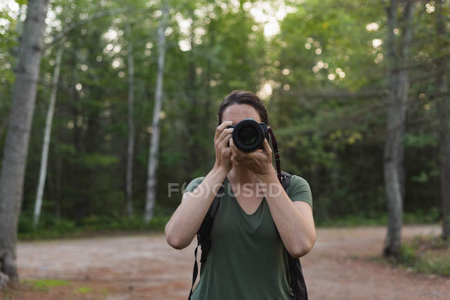 Mujer haciendo clic en fotos con cámara en el bosque - foto de stock