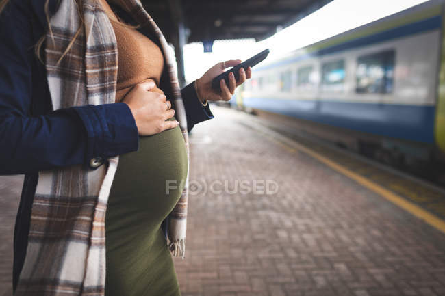 Mid section of pregnant woman using mobile phone at railway station — Stock Photo