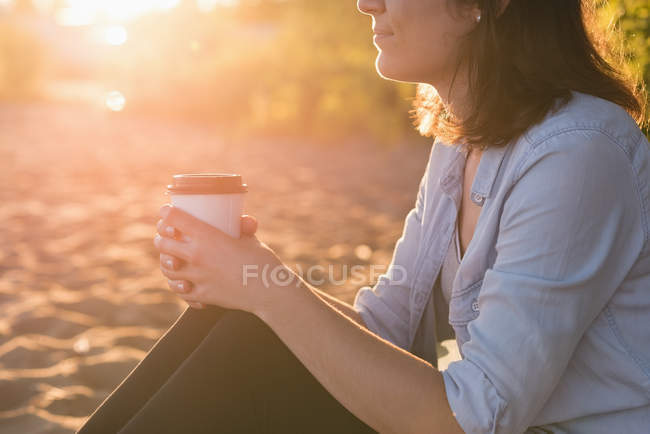 Mid section of woman holding a coffee cup near riverside — Stock Photo