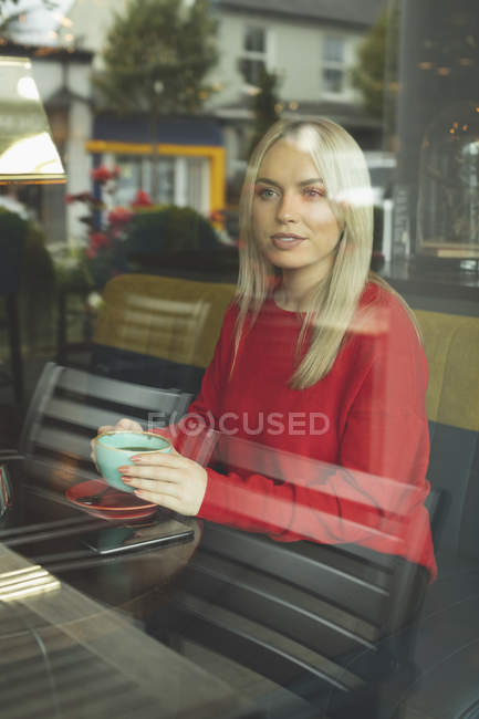 Женщина смотрит в окно, когда пьет кофе в кафе — стоковое фото