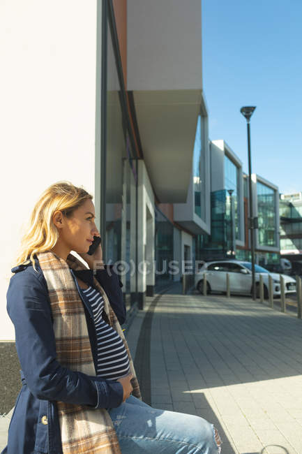 Donna incinta che parla al cellulare in città in una giornata di sole — Foto stock