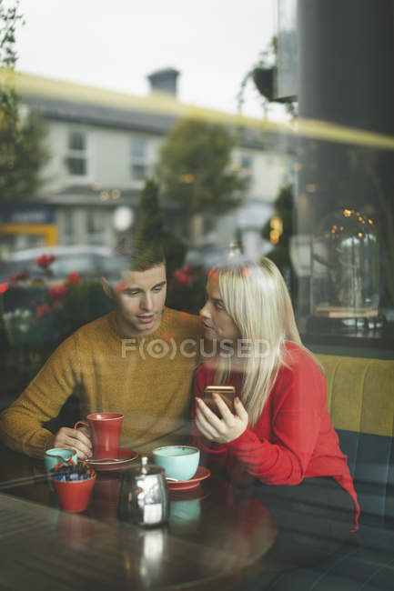 Junges Paar diskutiert mit Handy im Café — Stockfoto
