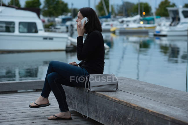 Vista lateral de la mujer hablando en el teléfono móvil cerca del puerto - foto de stock