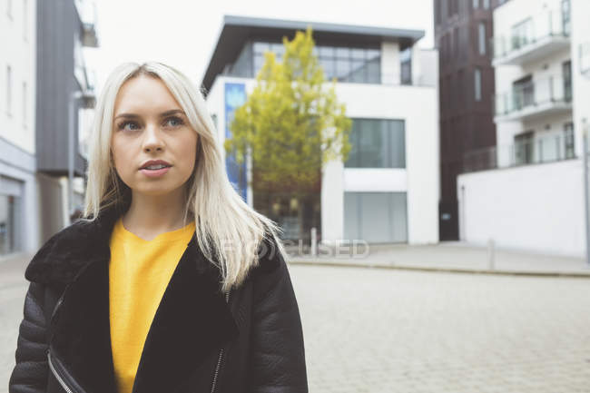 Femme blonde regardant loin tout en se tenant en ville — Photo de stock