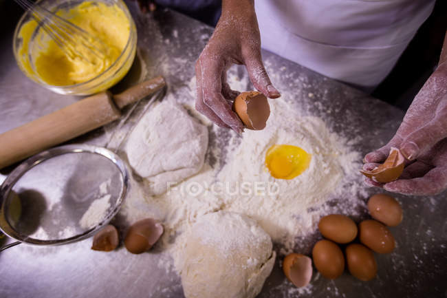 Sección media del chef que agrieta el huevo sobre la harina - foto de stock