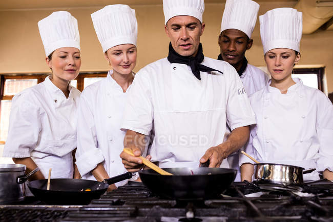 Chef cuisinier enseignant à son équipe à préparer un repas dans la cuisine — Photo de stock