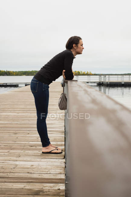 Вдумлива жінка стоїть на причалі біля берега річки — стокове фото