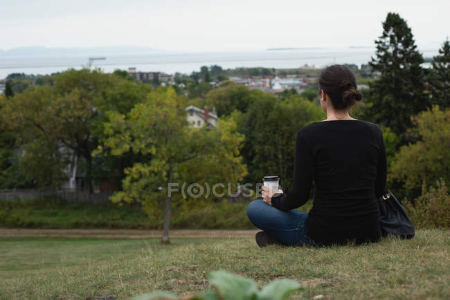 Rear view of woman having coffee while sitting on a hill — Stock Photo