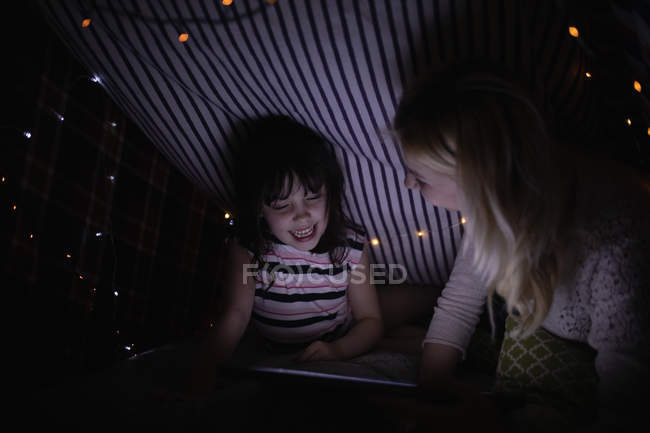 Mother and daughter using digital tablet under blanket at home — Stock Photo